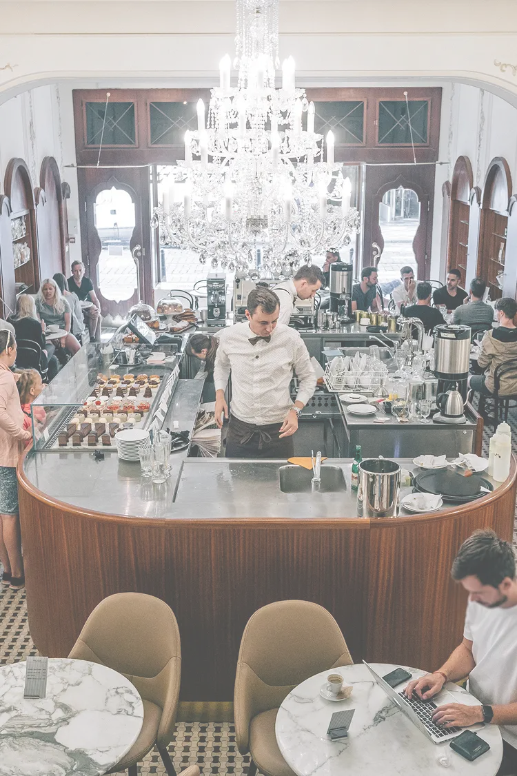 Interior of Myšák patisserie with central counter and guests.