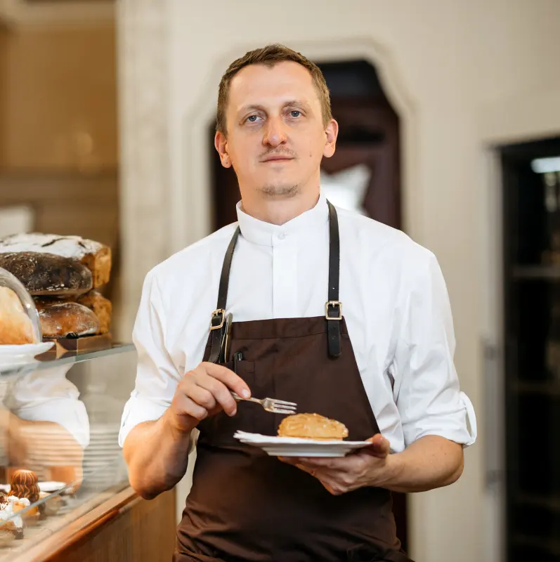 Pastry chef at Myšák pastry shop holding a dessert by the display case.