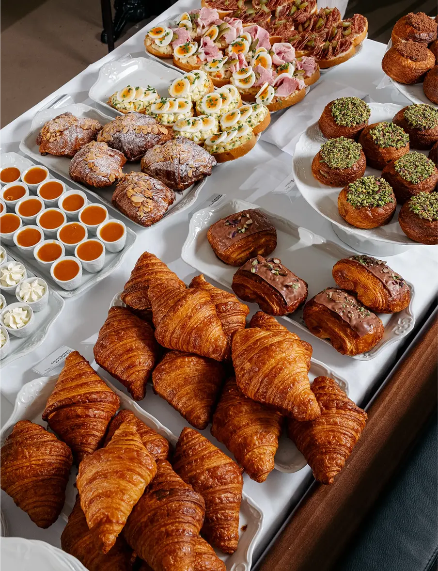 Selection of sweet pastries at Myšák pastry shop, including croissants, cakes, and desserts on porcelain trays.